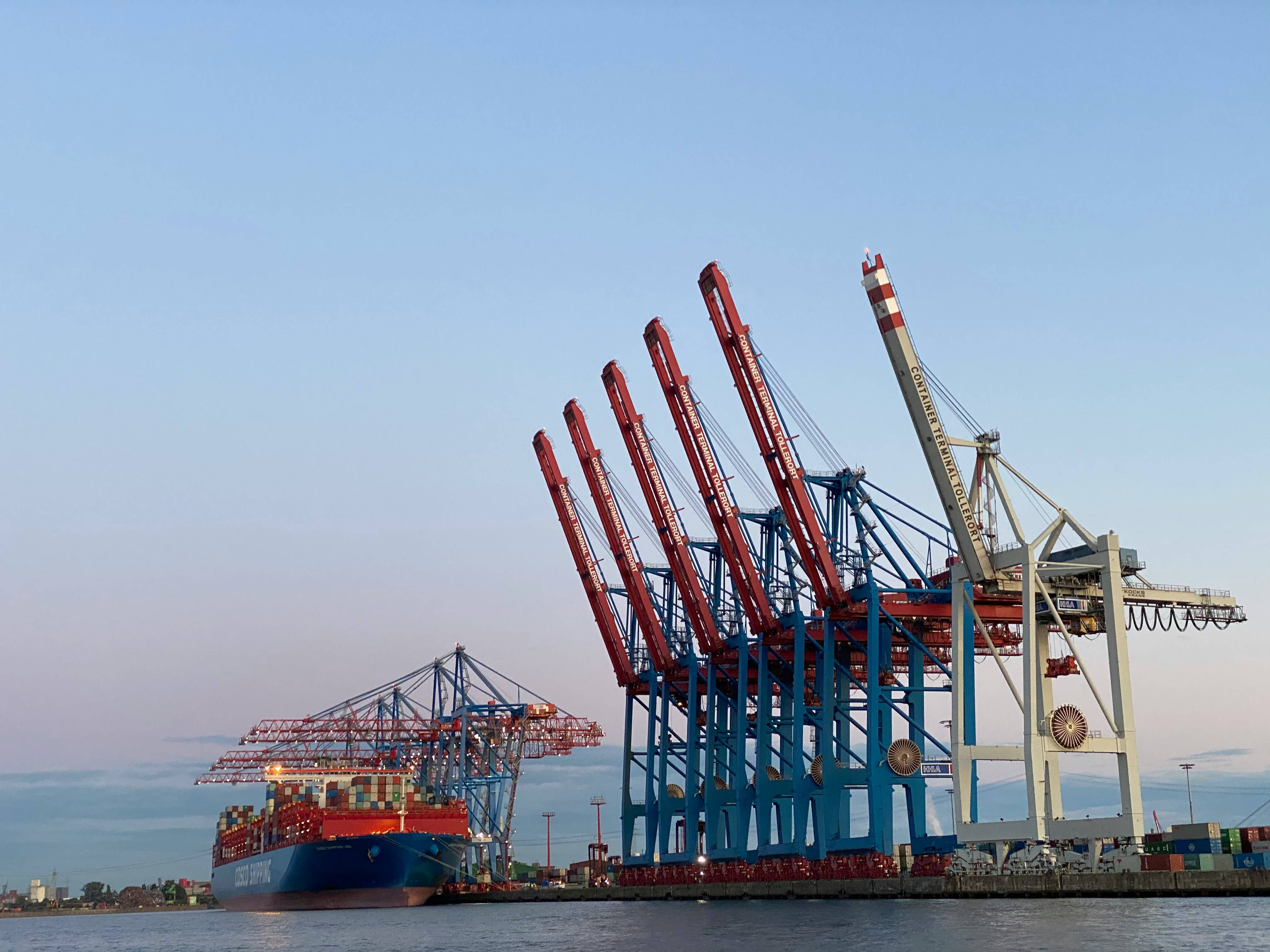 COSCO Shipping vessel at dusk beneath port cranes during a cleared cargo operation