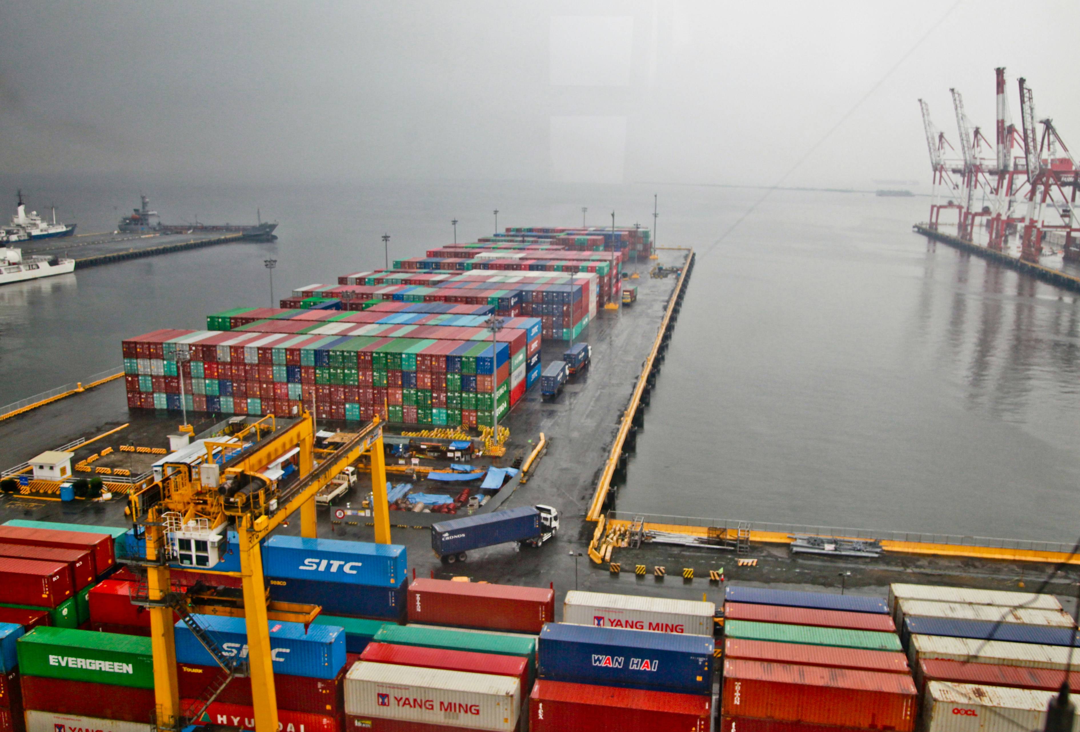 Rainy container terminal with a loaded vessel deck during a cross-stuffing cargo transfer