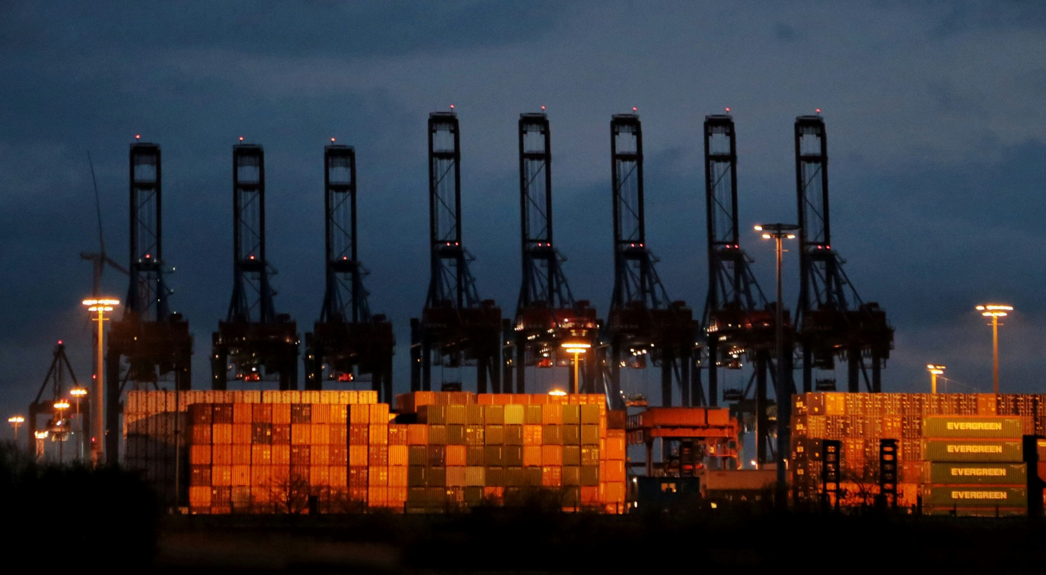 Silhouetted gantry cranes at dusk over stacked containers, reflecting sustainable port operations